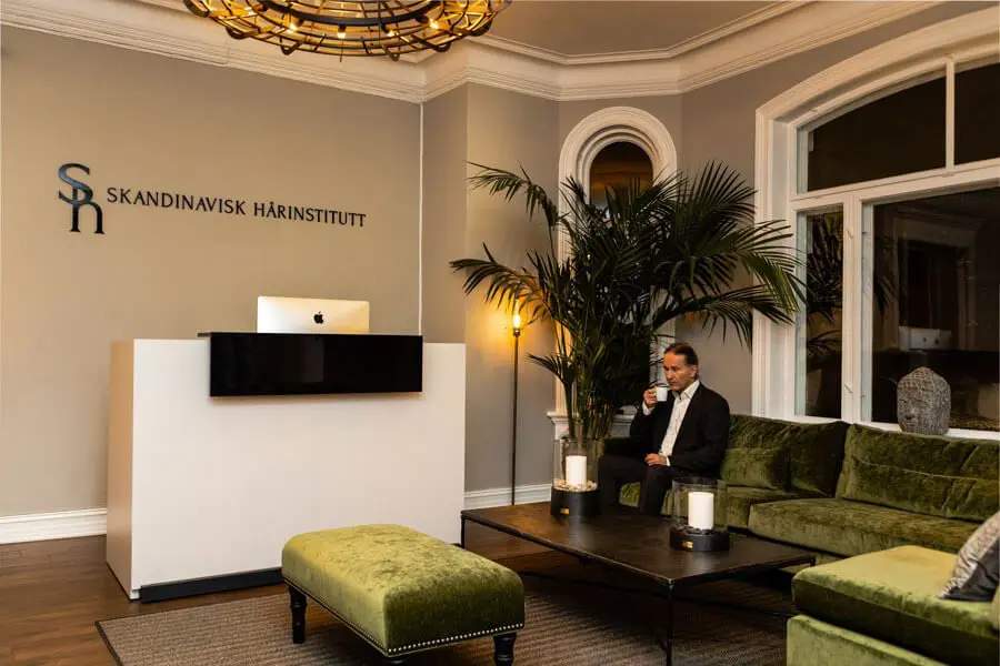 Resepsjonen og venterommet på klinikken med grønne sofaer. En mann som venter på sin tur og drikker kaffe.