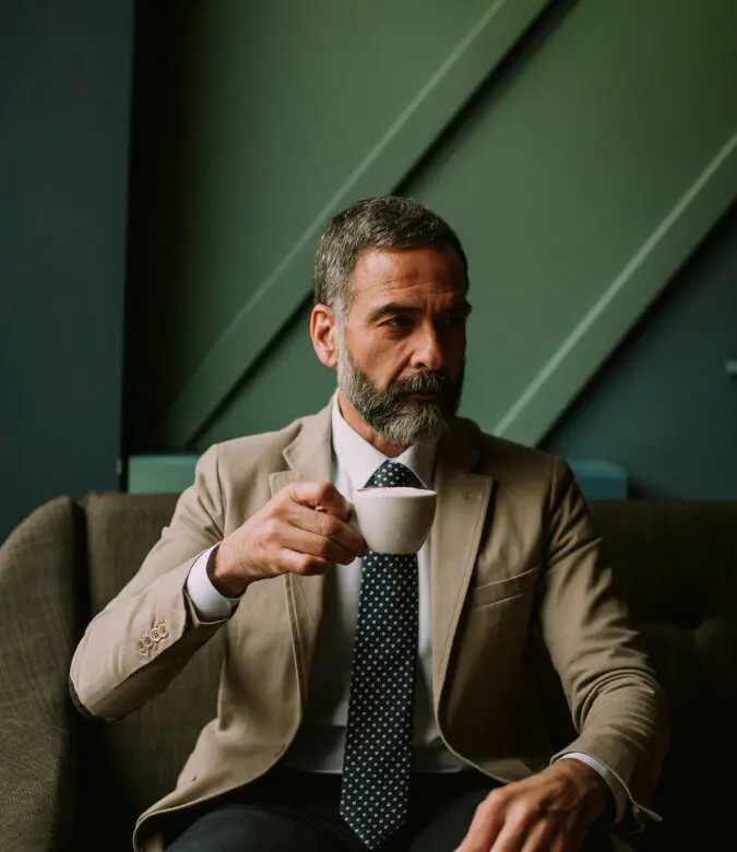Mann med grått hår og skjegg som holder en kaffekopp.