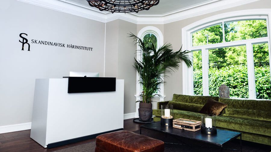service2 Venterom/resepsjon til klinkken. Grønne sofaer, med svart kaffebord. Stor vinduer som gir naturlig lys. Grønne planter i en buddah vase.