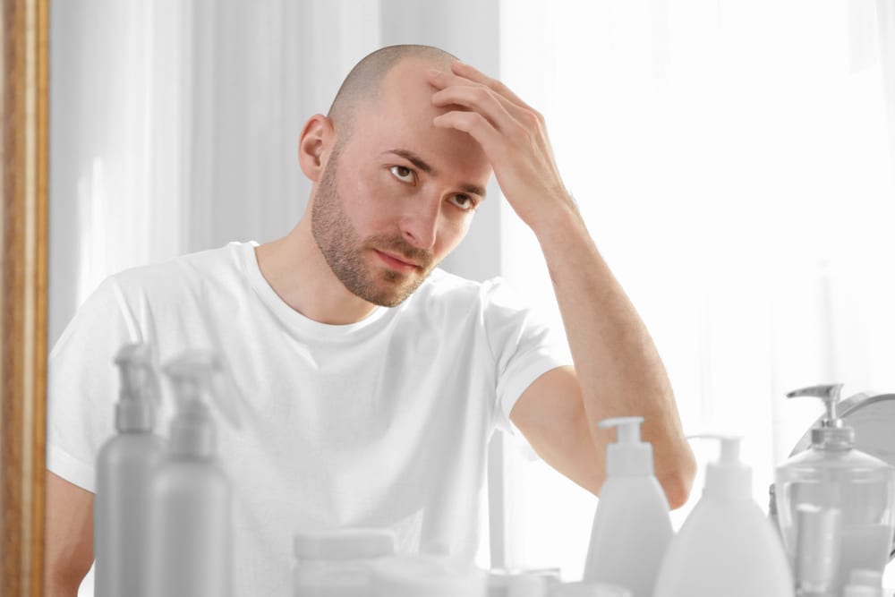 shutterstock_615402602 Mann tar på hodebunnen sin og ser på seg selv i speilet.