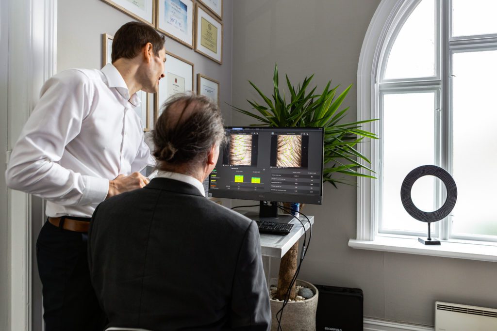 Hudlege viser sin pasient et bilde av håret hans på en datamaskin.