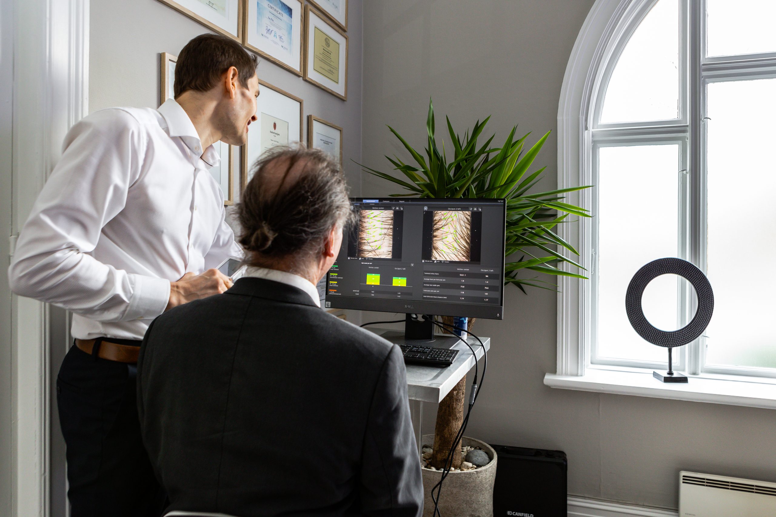 Hårkirurg viser bilde av pasienten sitt hår. Pasient ser på pc skjermen.