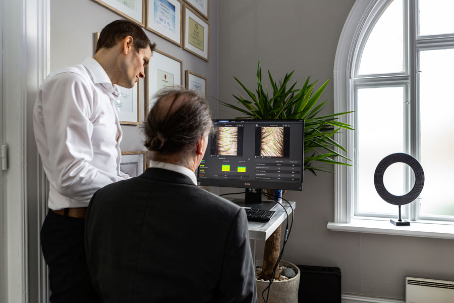Kirurg viser en mannlig pasient et bilde av håret hans på en datamaskin.