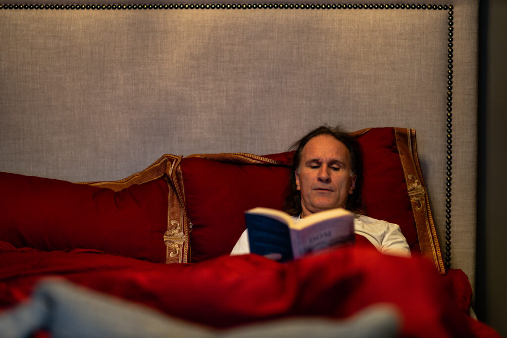 Mann som leser bok i en seng. 