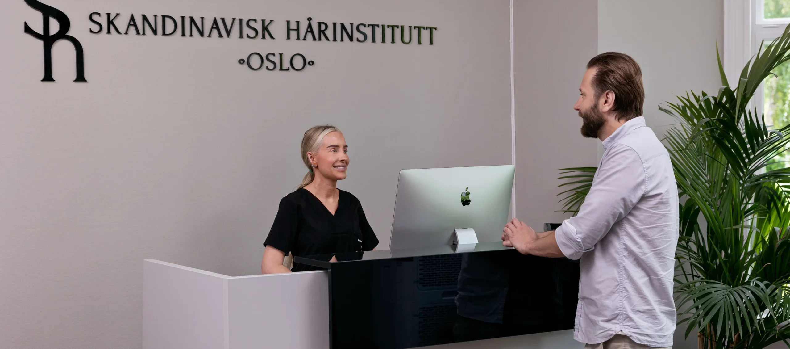 Mann som prater med resepsjonisten hos Skandinavisk Hårinstitutt.