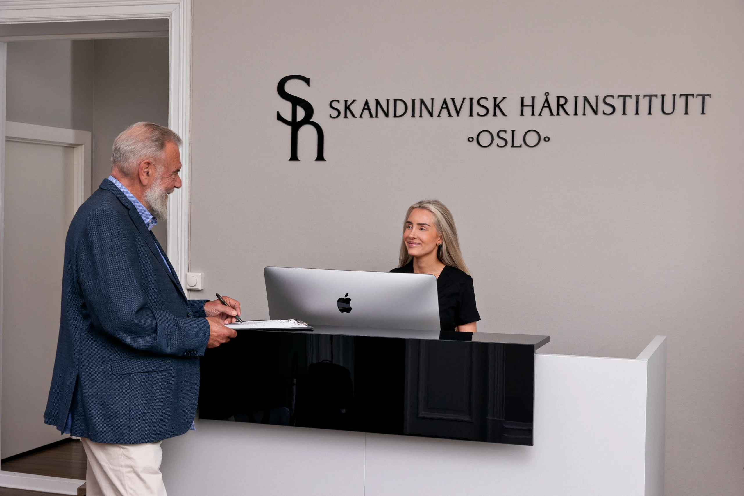 Eldre mann som prater med resepsjonisten hos Skandinavisk Hårinstitutt.