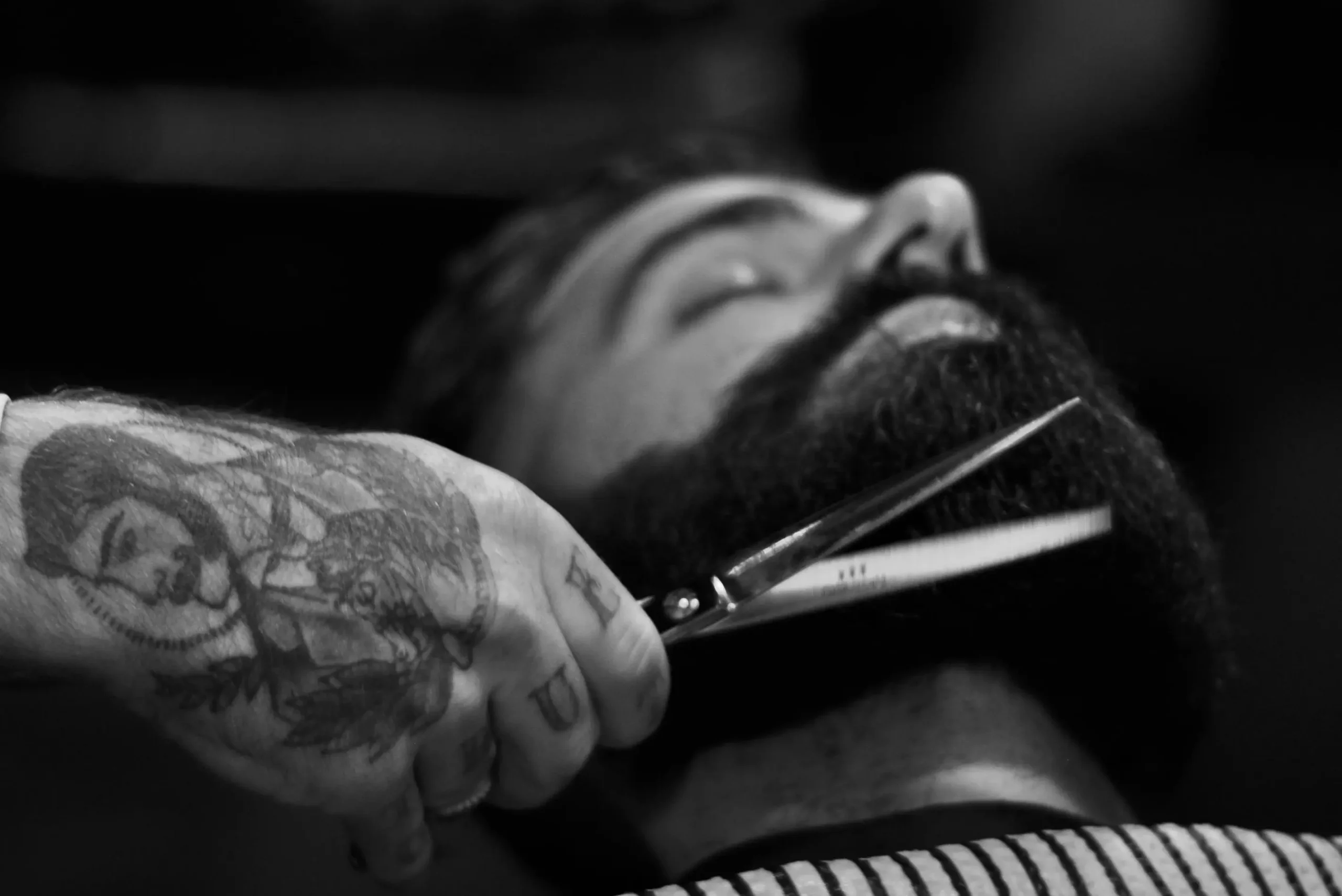 Person som klipper skjegget til en mann med saks. 